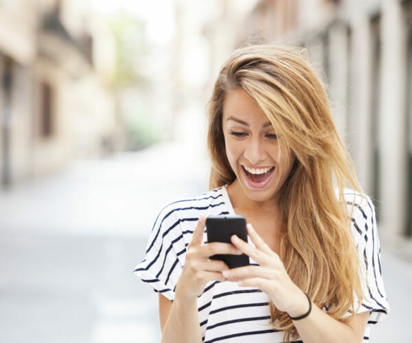 Portrait of a smiling beautiful woman typing on the smart phone with city unfocused background